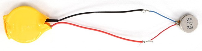 The leads of a coin cell battery and a vibration motor are soldered together in a closed circuit