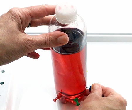 A hand gently holding the bottle while another hand pulls a pin out of the bottle.