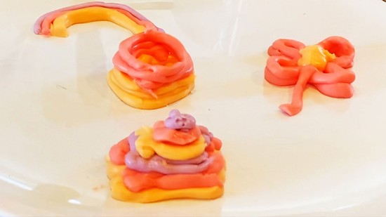  Four shapes printed from icing  - a layered pyramid, a square tower, a rainbow, and a flower - on a plate.  