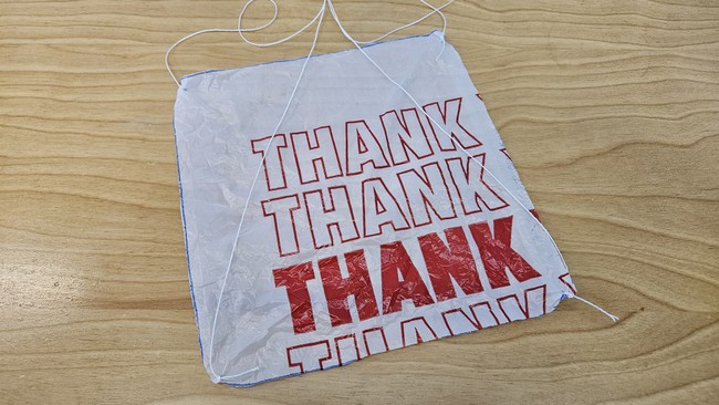 square plastic bag parachute with a string tied to each corner