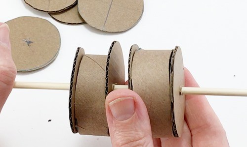 Two units consisting of a circle pressed against a section of cardboard tube and a second circle sitting on one skewer.