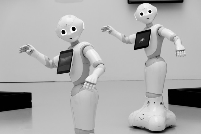 Two humanoid white plastic robots. They have eyes, mouths, mostly human-shaped bodies, and arms with hands and fingers.