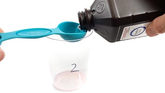 A person fills a tablespoon with hydrogen peroxide.