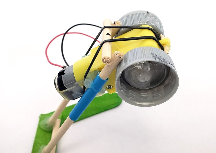 A rubber band looped over one end of the motor, up over the crossbar, and hooked to the other end of the motor.