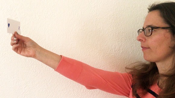 A person extending her right arm while holding a paper card at eye level in her right hand.