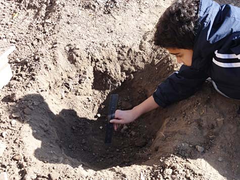 Student using a ruler to measure the depth of a hole that is about 1 foot deep