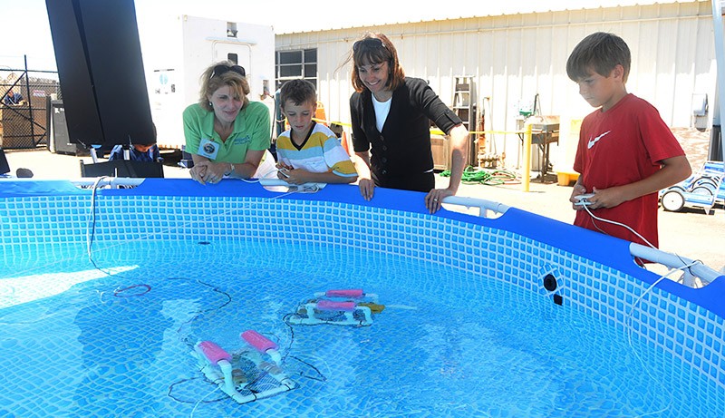 People standing next to a pool while controlling two SeaPerch robots 