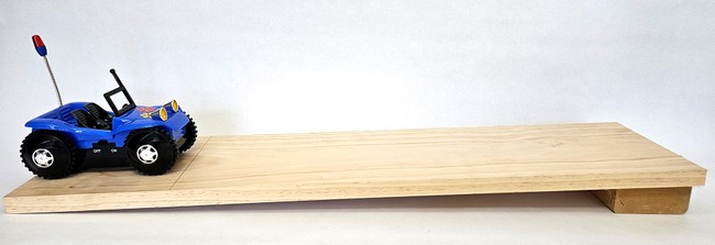 Toy car on a ramp made from a board with one end propped up slightly on a block of wood