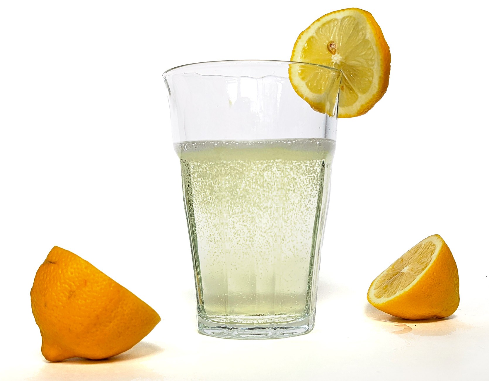 Fizzing yellow lemonade in a clear glass surrounded by sliced lemons.