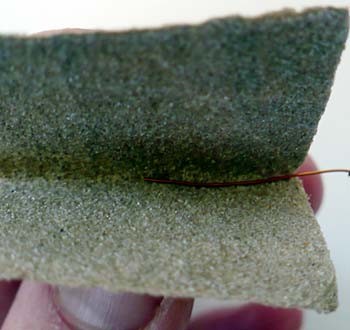 Sandpaper is used to remove insulation from the end of a magnet wire