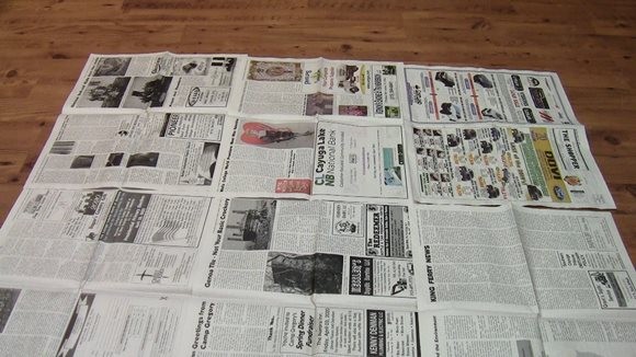 A wood floor covered in a grid of newspaper.