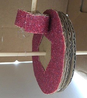 A circle spiraling out treaded on an axle with a flat piece of cardboard resting on the spiral.