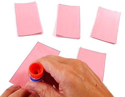 Three paper strips on a table. Hands holding a gluestick and applying glue to an additional paper strip.