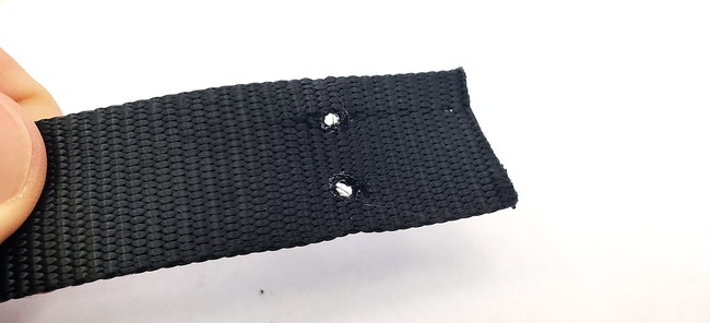 The end of a buckle strap with two holes, each about 1 inch from the end and 1/4 inch in from the edges. 