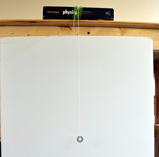 A small metal washer is suspended from a string that is tied to the end of a ruler