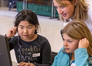 A teacher helping two students in front of a computer