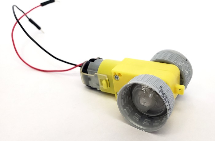 Motor with a shaft sticking out each side. Bottle caps with holes drilled into them are pressed onto the shafts and glued in place.