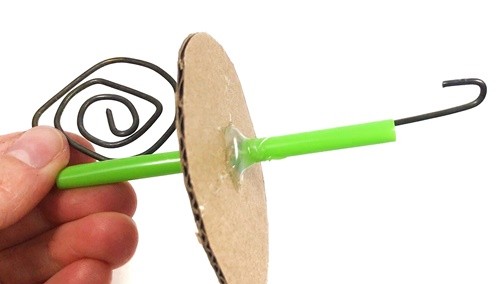 Metal wire stuck through a cardboard circle with a spiral on one end and a hook on the other.