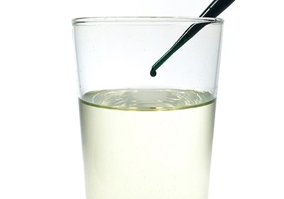 A pipette is adding one drop of water-food coloring mixture to a glass filled with cooking oil.
