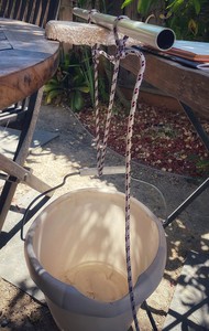 A picture of a panel, its sides barely resting on the edges of two tables. A dowel rests on the panel, parallel with the gap between the tables.  A bucket hangs under the panel, it is attached to the dowel with rope.  