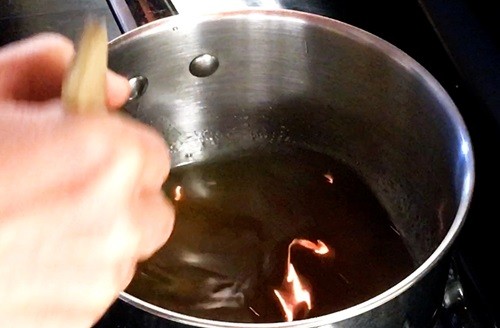 Person stirring in a saucepan containing translucent sugar syrup.