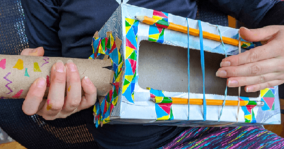 Student holding rubber band guitar made from cardboard box