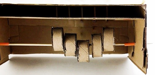 Axle with the driving cylinders attached threaded through two pieced of straw that stick out from either side panel into the box