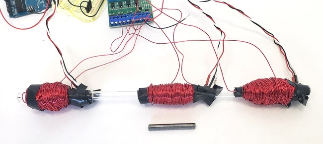 A clear plastic tube with three large wire coils wrapped around it