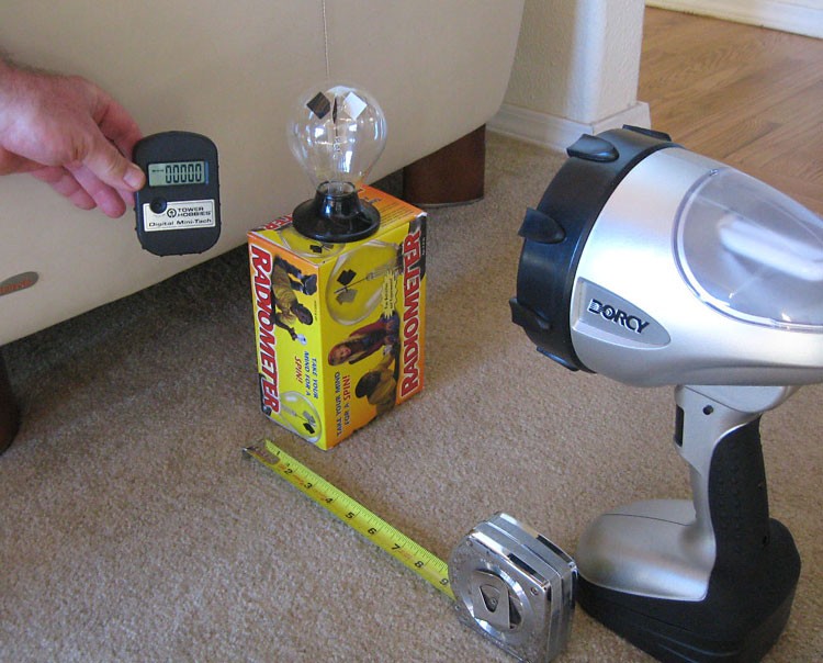 Person using a tachometer to measure the rotation rate of vanes of a radiometer exposed to a spot light