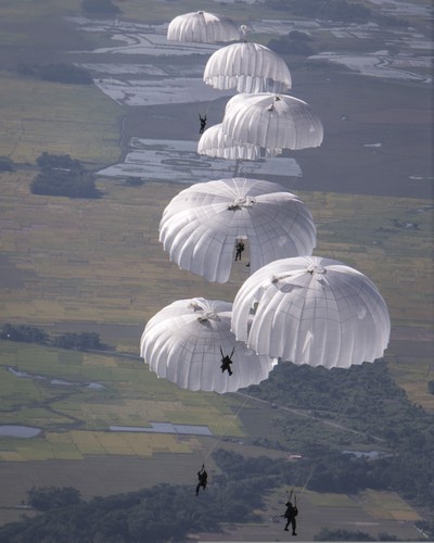 Multiple paratroopers falling through the sky with their parachutes deployed
