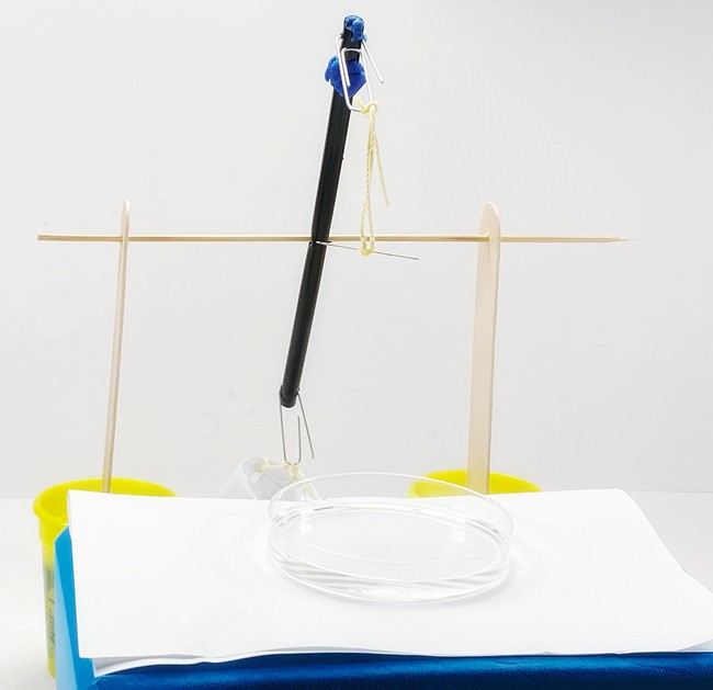 the surface tension measurement tool with the beam tipped over so the needle hangs in the air, far above the surface of the water.