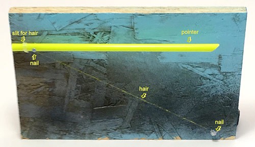 A hair is stretched from one corner of a wood board to the end of a straw at the opposite corner of the board