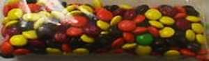 Clear bag full of yellow, brown, orange, and red M&Ms in near equal proportions and only one green M&M.