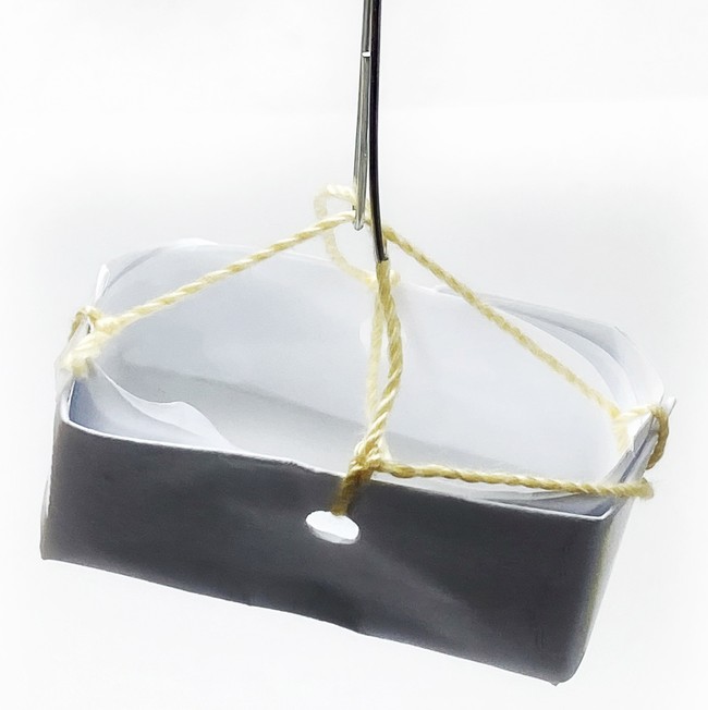 A basket folded from paper coated with tape. Four string hang the basket from a metal hook.