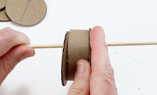 A short section of cardboard tube being pressed against a circle. The circle and the tube are both threaded on a skewer.