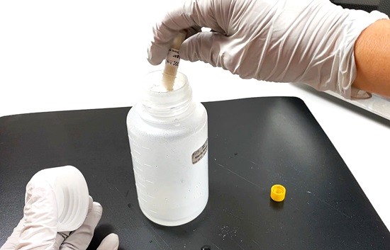 A person with gloved hands is pouring LB agar powder into an open bottle.