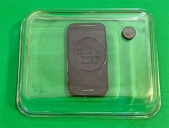 An upside down glass dish protects a smartphone from a magnet above
