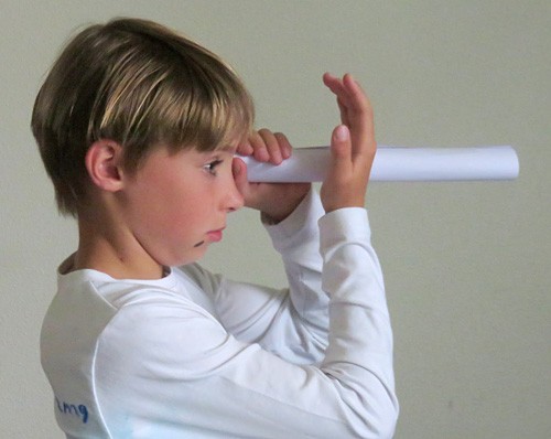 A child looks through a long paper tube with one eye and holds a hand in front of their other eye