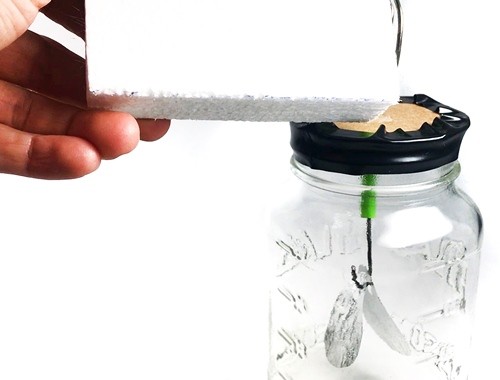 Person holding a Styrofoam piece and touching the metal coil of the homemade electroscope with the Styrofoam.
