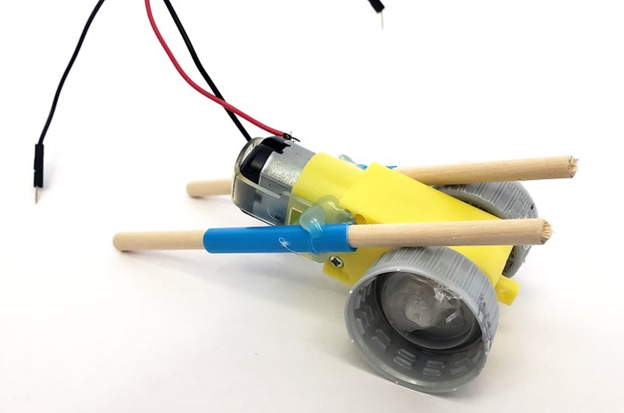 Each side of the motor has a straw glued to it at an angle. A wooden dowel goes through each straw and rests against the bottle cap wheel.