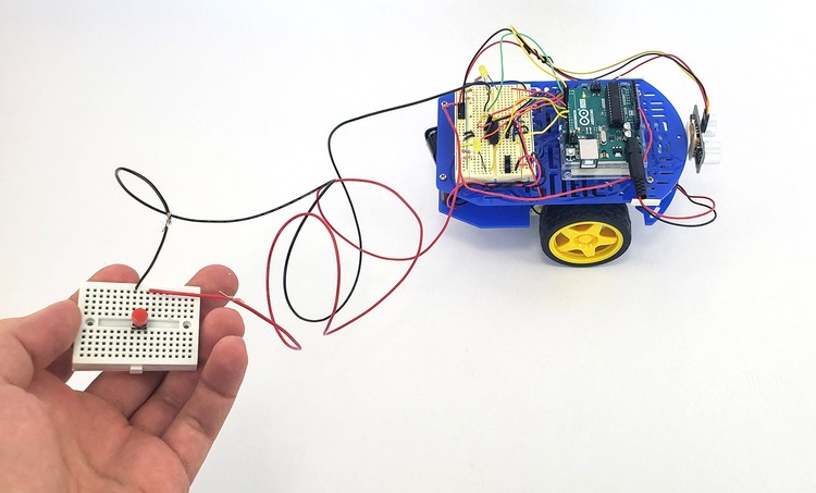  A hand holds a mini breadboard remote wired to a robot vehicle.