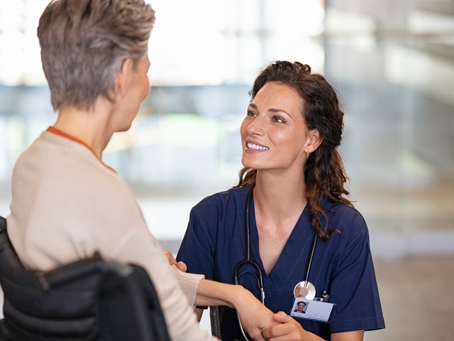 A nurse assistant and an older woman smiling at each other.