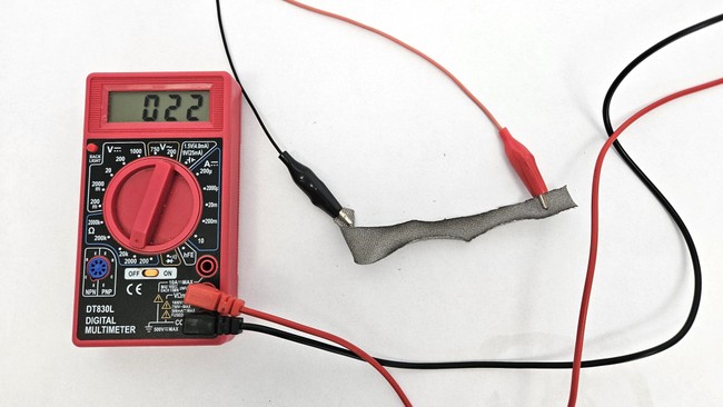 a strip of conductive fabric connected to a multimeter to measure its resistance