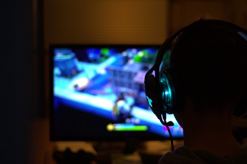 the back of a person's head (wearing head phones) with a video game on a screen in the background