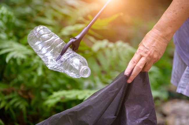 A person picking up a plastic bottle with a trash grabber