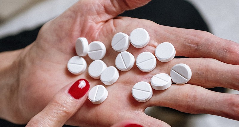 Hands of an elderly woman with many white pills across her palm.