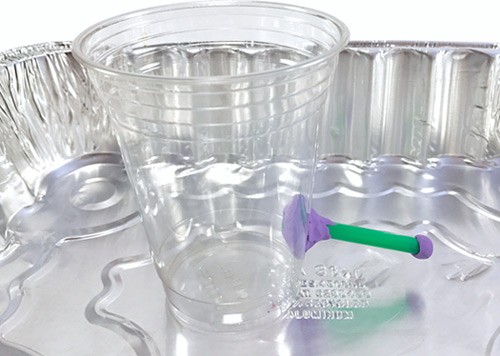 A plastic cup with a straw spout near the bottom sits in an aluminum pan