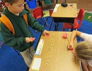 A student picks up a small square of paper from the corner of another students desk
