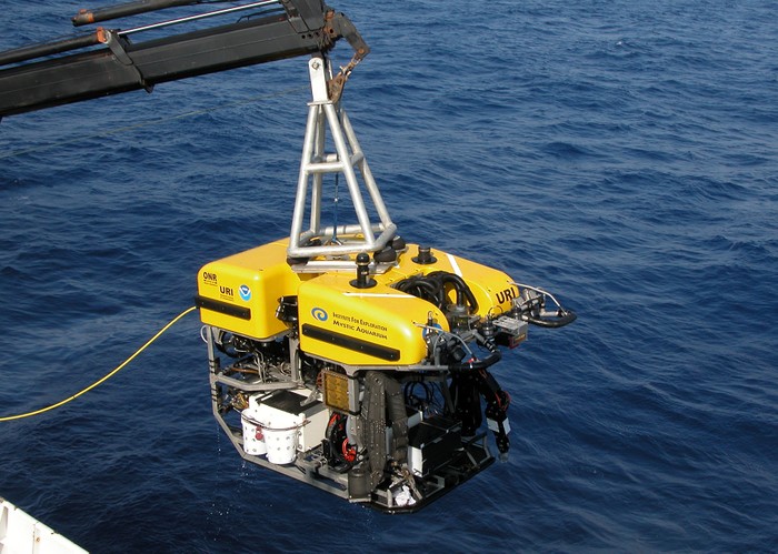 an ROV suspended from a crane over the side of a boat.