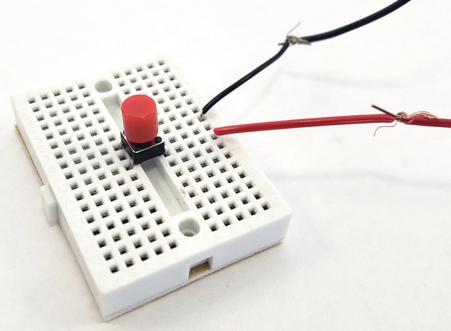 A button on a mini breadboard with two external wires connected 